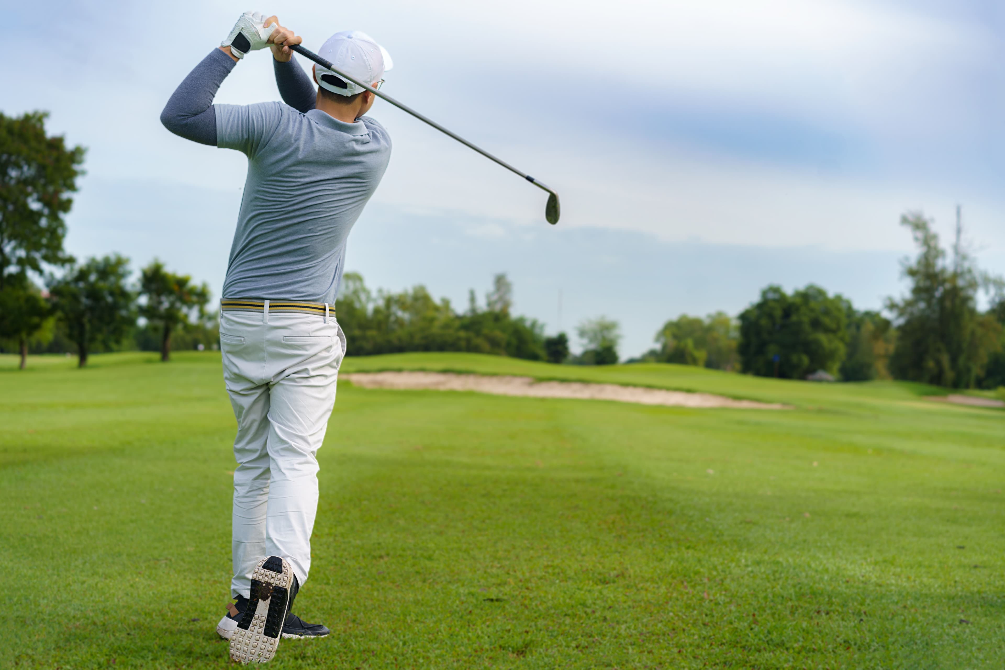 Asian man golfer hitting golf ball along fairway with iron driver